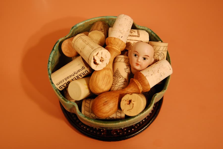 Photo of a small bald baby doll head mixed in with a bowl of wine bottle corks